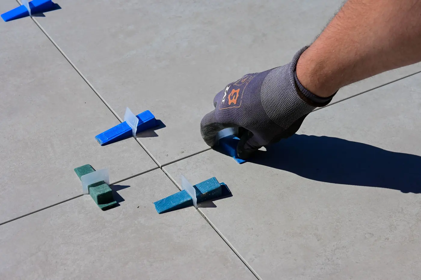 Une main gantée place des croisillons entre de grands carreaux gris